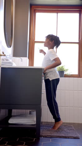 Video-Vertical-De-Un-Niño-Afroamericano-Cepillándose-Los-Dientes-En-El-Baño-De-Casa,-Cámara-Lenta