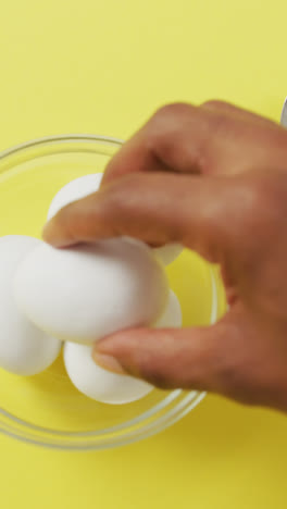Video-of-close-up-of-biracial-man-putting-egg-into-bowl-on-yellow-background