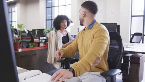 Happy-diverse-male-and-female-colleagues-working-at-desks,-passing-document-and-talking,-slow-motion