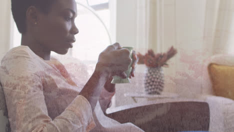 Animation-of-winter-landscape-over-african-american-woman-drinking-coffee