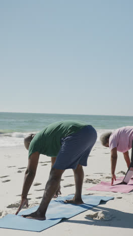 Video-Vertical-De-Una-Pareja-Afroamericana-Haciendo-Yoga-En-La-Playa,-En-Cámara-Lenta