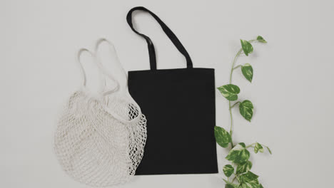 Close-up-of-white-and-black-bags-with-green-plant-on-white-background,-with-copy-space,-slow-motion