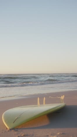 Vertical-video-of-surfboard-on-beach,-in-slow-motion,-with-copy-space