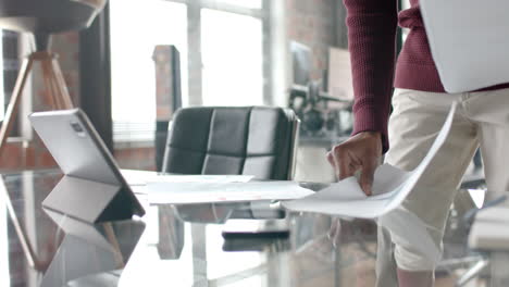 Midsection-of-african-american-casual-businessman-looking-at-documents-in-office,-slow-motion