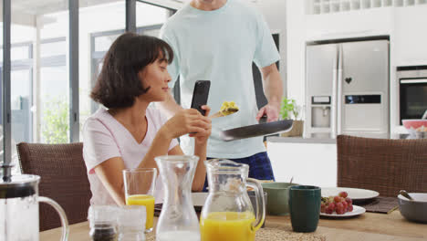 Video-of-happy-diverse-couple-preparing-breakfast-together-in-kitchen