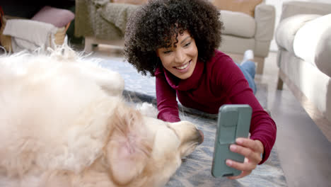 Mujer-Birracial-Feliz-Tomando-Fotos-Con-Un-Perro-Golden-Retriever-Usando-Un-Teléfono-Inteligente-En-Casa,-Cámara-Lenta