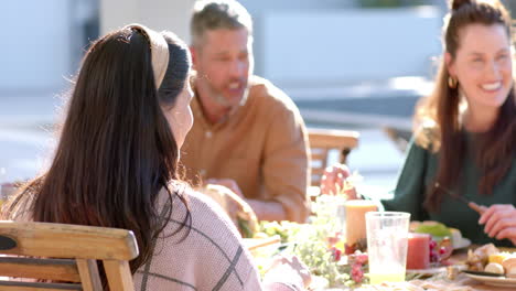 Happy-diverse-male-and-female-friends-eating-thanksgiving-celebration-meal-in-sunny-garden