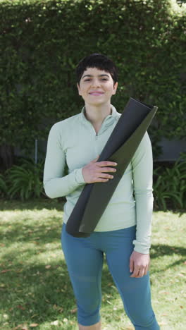 Happy-caucasian-woman-standing-with-yoga-mat-and-smiling-in-sunny-garden,slow-motion