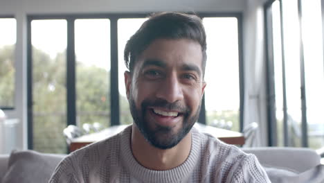 Portrait-of-happy-biracial-man-sitting-on-sofa-smiling-at-home,-slow-motion