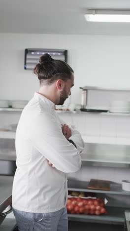 Caucasian-male-chef-standing-with-arms-crossed-in-kitchen,-slow-motion,-vertical