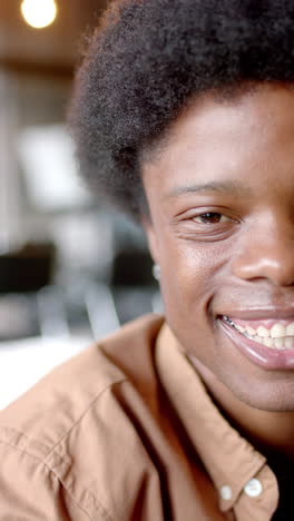 Vertical-video-of-portrait-of-happy-african-american-man-sitting-on-sofa-at-home,-slow-motion