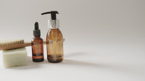 Close-up-of-glass-bottles-with-pumps,-soap,-brush-and-copy-space-on-white-background