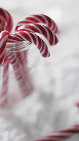 Vertical-video-of-christmas-candy-canes-in-glass-jar-and-copy-space-on-snow-background