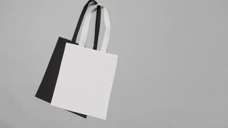 Close-up-of-white-and-black-bags-on-grey-background,-with-copy-space,-slow-motion