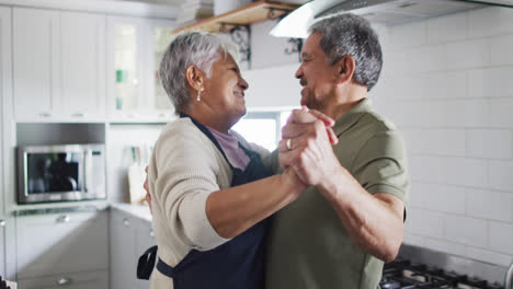 Happy-senior-biracial-couple-dancing-in-kitchen