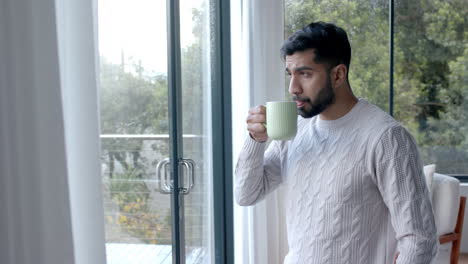 Hombre-Birracial-Pensativo-Tomando-Café-Y-Mirando-Por-La-Ventana-En-Casa,-Cámara-Lenta