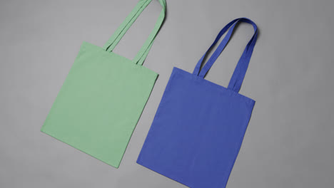 Primer-Plano-De-Bolsas-Verdes-Y-Azules-Sobre-Fondo-Gris,-Con-Espacio-Para-Copiar,-Cámara-Lenta