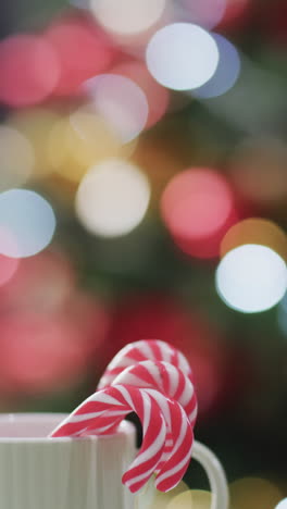 Vertical-video-of-christmas-candy-canes-in-mug,-christmas-tree-and-copy-space