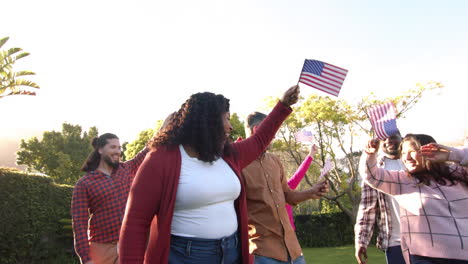 Happy-diverse-male-and-female-friends-dancing-with-flags-in-sunny-garden