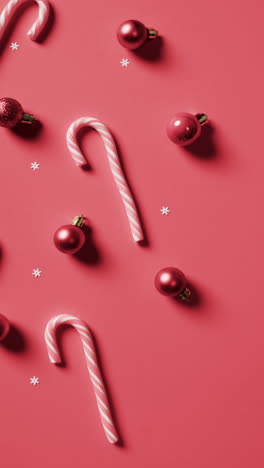 Vertical-video-of-candy-canes,-red-baubles-christmas-decorations-with-copy-space-on-red-background