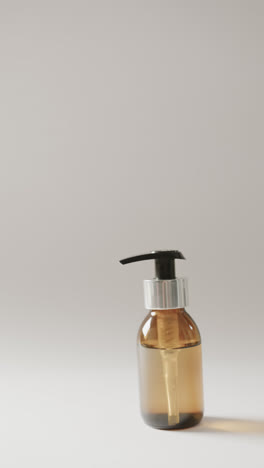 Vertical-video-of-close-up-of-glass-bottle-with-pump-and-copy-space-on-white-background