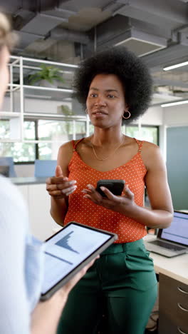 Vertical-video-of-diverse-female-creative-colleagues-discussing-using-tablet-in-office,-slow-motion