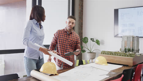 Diverse-male-and-female-architects-with-tablet-discussing-blueprints-standing-in-office,-slow-motion