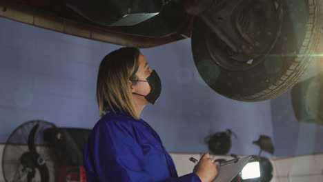 Animation-of-light-spots-over-biracial-woman-with-face-mask-repairing-car