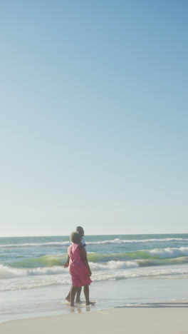 Vertical-video-of-senior-african-american-couple-walking-at-beach,-in-slow-motion