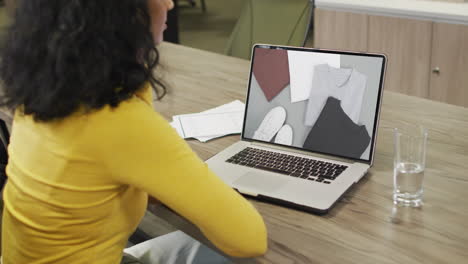 Biracial-woman-at-table-using-laptop,-online-shopping-for-clothes,-slow-motion