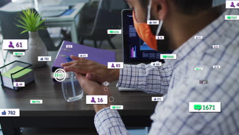 Animation-Von-Social-Media-Symbolen-über-Einem-Mann-Mit-Gemischter-Abstammung,-Der-Eine-Gesichtsmaske-Trägt-Und-Im-Büro-Ein-Händedesinfektionsmittel-Verwendet