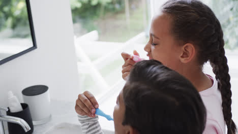 Happy-biracial-brother-and-sister-brushing-teeth-in-sunny-bathroom,-slow-motion