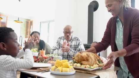 Happy-african-american-multi-generation-family-serving-food-at-thanksgiving-dinner,-slow-motion