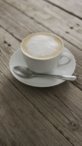 Vertical-video-of-cup-of-cappuccino-coffee-with-foamed-milk-on-wooden-table