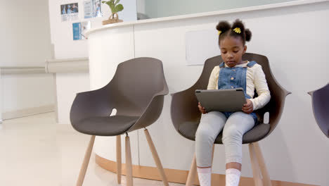 Happy-african-american-girl-sitting-in-hospital-waiting-room-and-using-tablet,-slow-motion