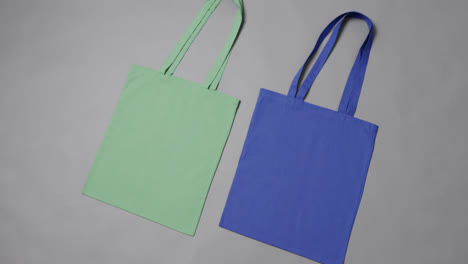 Primer-Plano-De-Bolsas-Verdes-Y-Azules-Sobre-Fondo-Gris,-Con-Espacio-Para-Copiar,-Cámara-Lenta