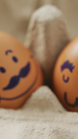 Video-Einer-Nahaufnahme-Von-Zwei-Braunen-Eiern-Mit-Gezeichneten-Gesichtern-Im-Eierkarton-Hintergrund