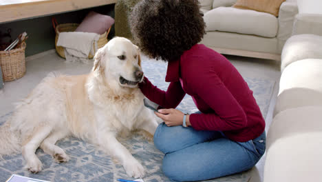 Feliz-Mujer-Birracial-Acariciando-A-Un-Perro-Golden-Retriever-Y-Usando-Un-Teléfono-Inteligente-En-Casa,-Cámara-Lenta