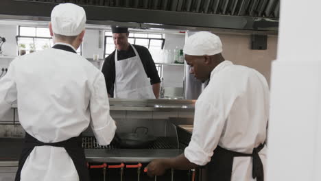 Focused-diverse-male-chef-instructing-trainee-male-chefs-in-kitchen,-slow-motion