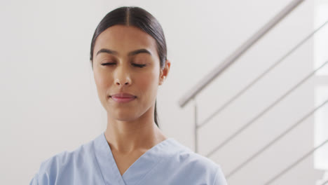 Video-of-happy-biracial-female-doctor-standing-at-stairs,-looking-at-camera