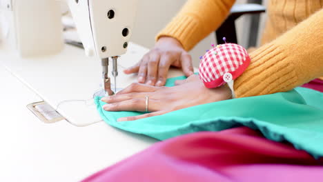 Diseñadora-De-Moda-Birracial-Cosiendo-Tela-Con-Máquina-De-Coser-En-Estudio,-Cámara-Lenta