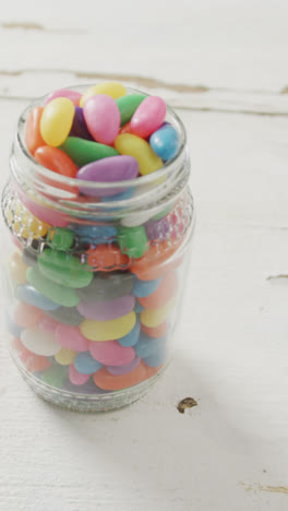 Video-of-overhead-view-of-multi-coloured-jelly-sweets-in-jar-over-white-rustic-background
