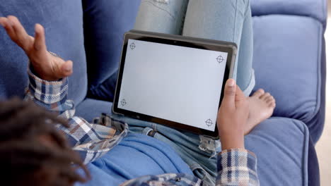 African-american-boy-using-tablet-with-copy-space-on-screen-lying-on-sofa-at-home,-slow-motion