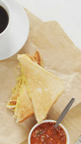 Video-of-coffee,-freshly-prepared-cheese-white-bread-sandwich-with-tomatoes-on-paper-and-white-plate