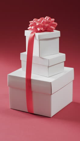 Vertical-video-of-stack-of-christmas-presents-and-copy-space-on-red-background