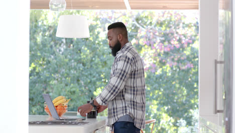 Focused-african-american-man-using-laptop-and-drinking-coffee-at-home,-slow-motion