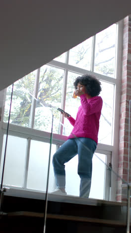 Video-Vertical-De-Una-Mujer-Birracial-Bebiendo-Té-Y-Usando-Un-Teléfono-Inteligente-En-Casa,-Cámara-Lenta