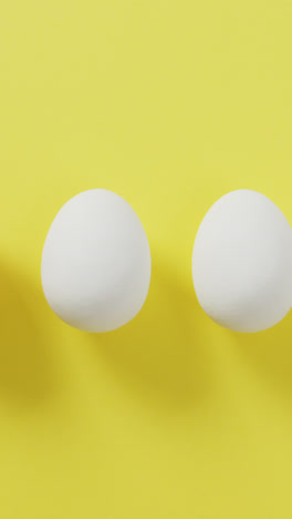 Video-of-row-of-one-brown-and-four-white-eggs-with-copy-space-on-yellow-background