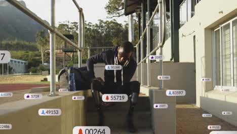 Animation-of-social-media-icons-over-african-american-man-adjusting-his-prosthetic-leg-at-stadium