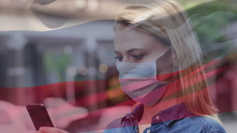 Animación-De-Ondear-La-Bandera-Rusa-Sobre-Una-Mujer-Caucásica-Con-Mascarilla-Usando-Un-Teléfono-Inteligente-En-La-Calle